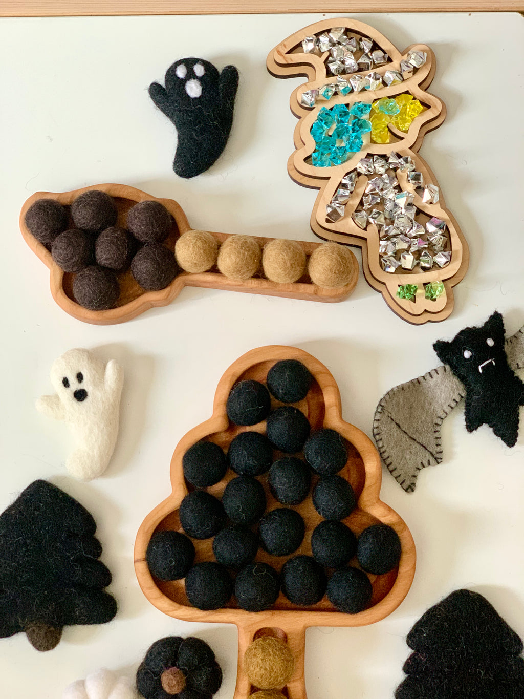 Wooden tree and leaf-shaped sensory trays filled with felt balls and surrounded by felt ghost and bat figures on white surface