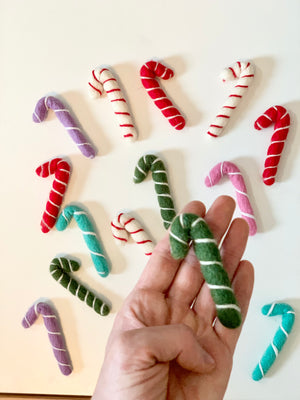 Hand holding a green felt candy cane with white stripes surrounded by assorted colorful felt candy canes on white background