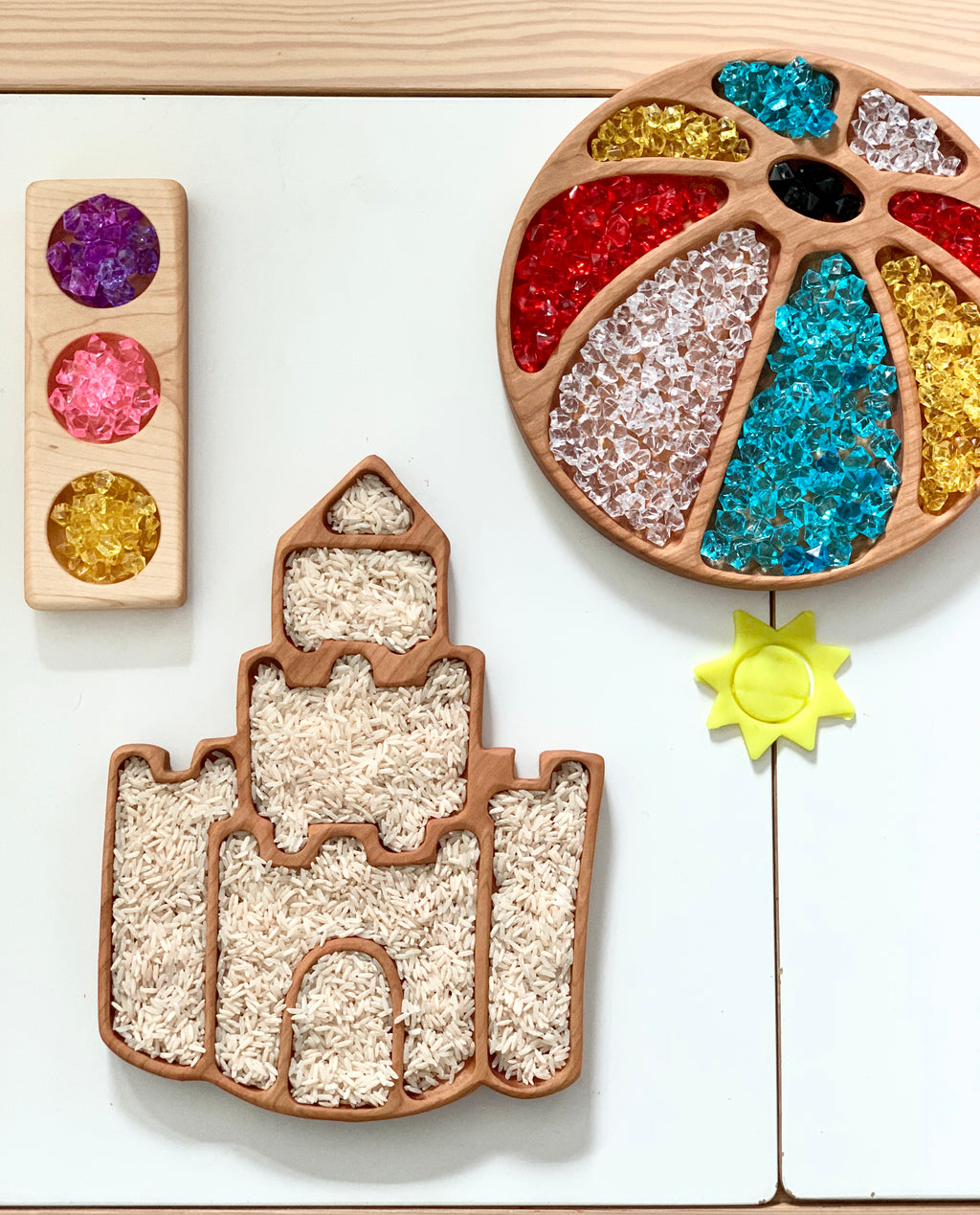 Wooden sensory trays shaped like a castle, circle with colorful translucent gems, and a rectangular traffic light with gem circles on white surface