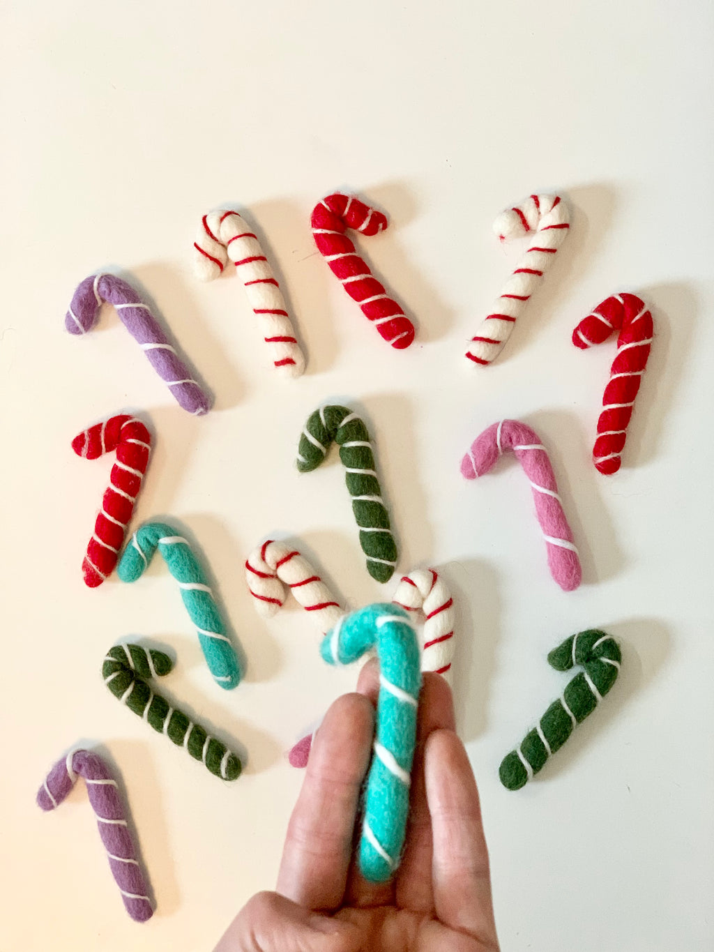 Assorted handmade felt candy canes in red, white, green, purple, and turquoise on white background with hand holding one