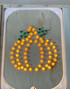 Wooden geometric board insert with warm orange lights shaped like a pumpkin with green leaf details on light wood surface