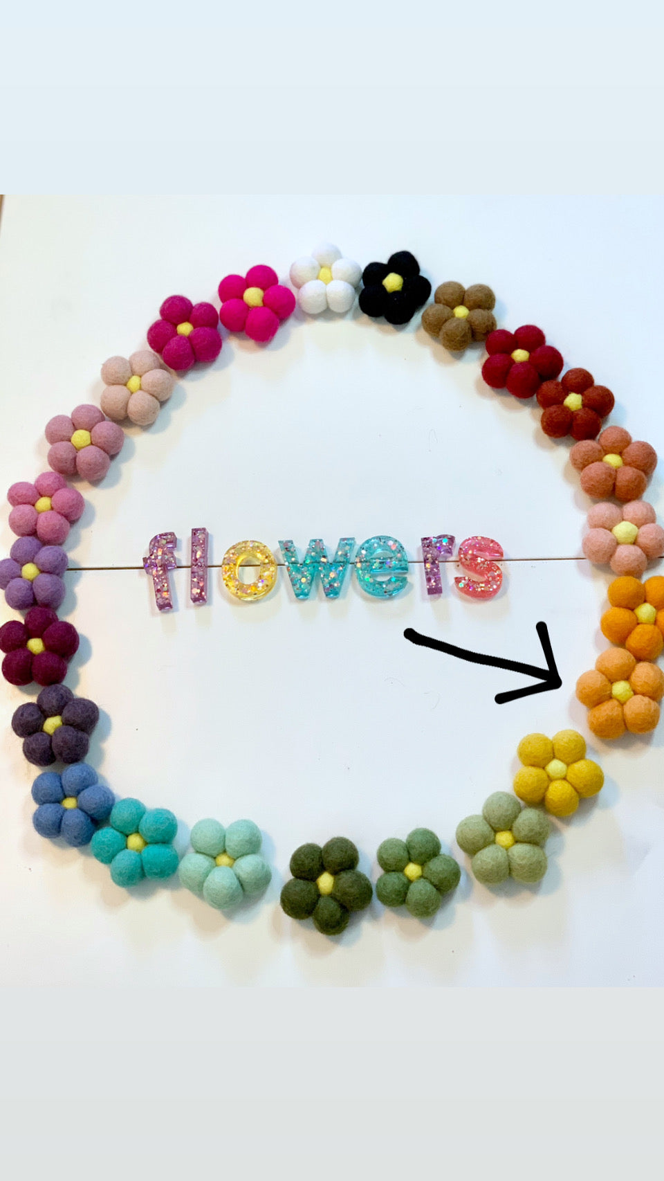 Circle of colorful handmade felt flowers with yellow centers and glittery letters spelling flowers on white background