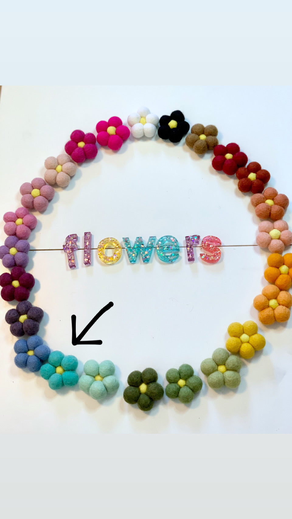 Circle of colorful handmade felt flowers with yellow centers surrounding glittery letters spelling flowers on white background
