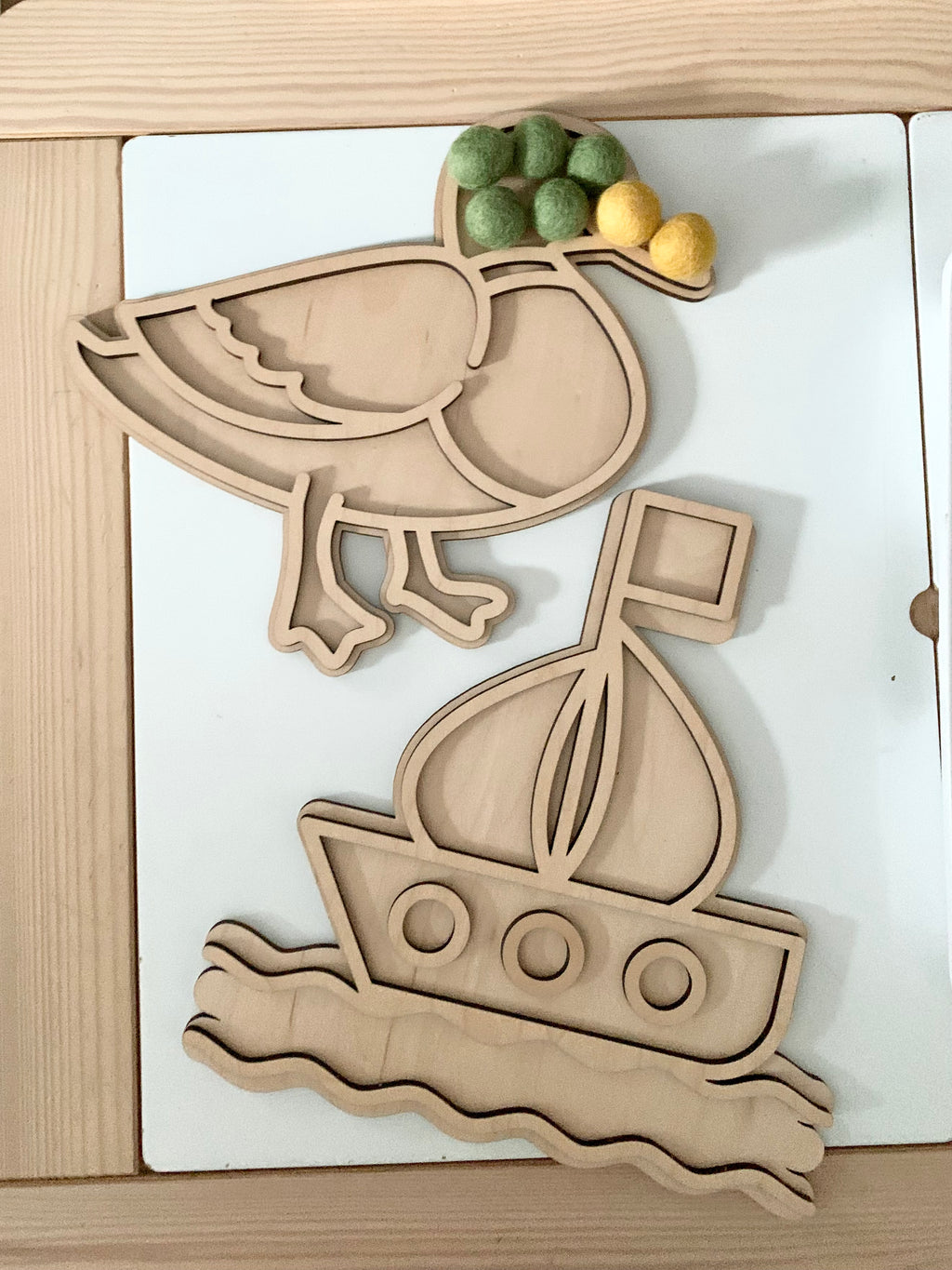 Wooden fillable bird and boat play trays with green and yellow felt balls on light wood and white background