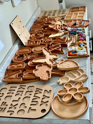Assorted natural wooden alphabet plates and sensory trays with carved letters and shapes laid out on marble surface