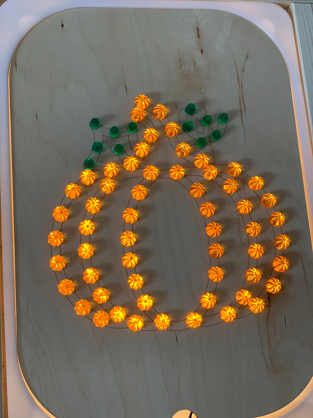 Wooden geometric board with orange pumpkin-shaped string lights and green leaf-shaped accents on light wood surface
