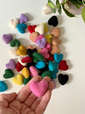 Assorted colorful small felt hearts handmade from 100% pure wool scattered on white surface with hand holding pink heart
