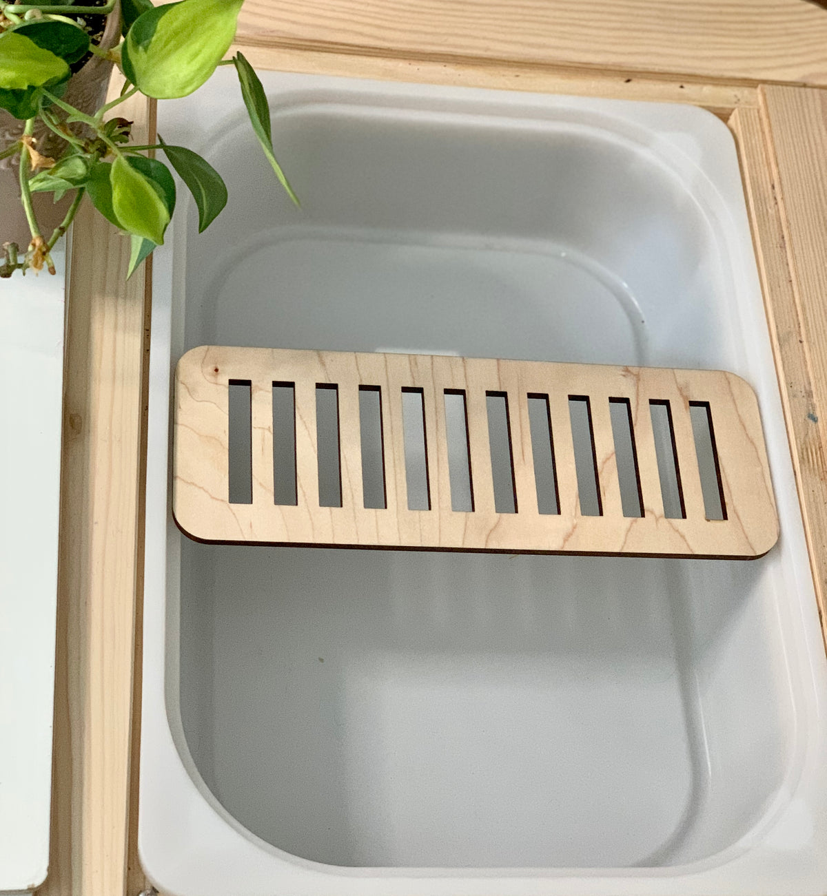 Maple plywood cross piece slot insert fitted inside Trofast Flisat bin with light green plant nearby on wooden surface