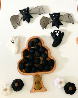 Tree-shaped wooden sensory tray filled with black felt balls, surrounded by felt bats, ghosts, and pumpkins on white surface