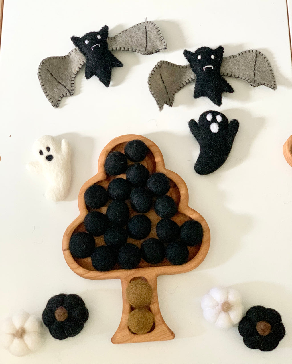 Tree-shaped wooden sensory tray filled with black felt balls, surrounded by felt bats, ghosts, and pumpkins on white surface