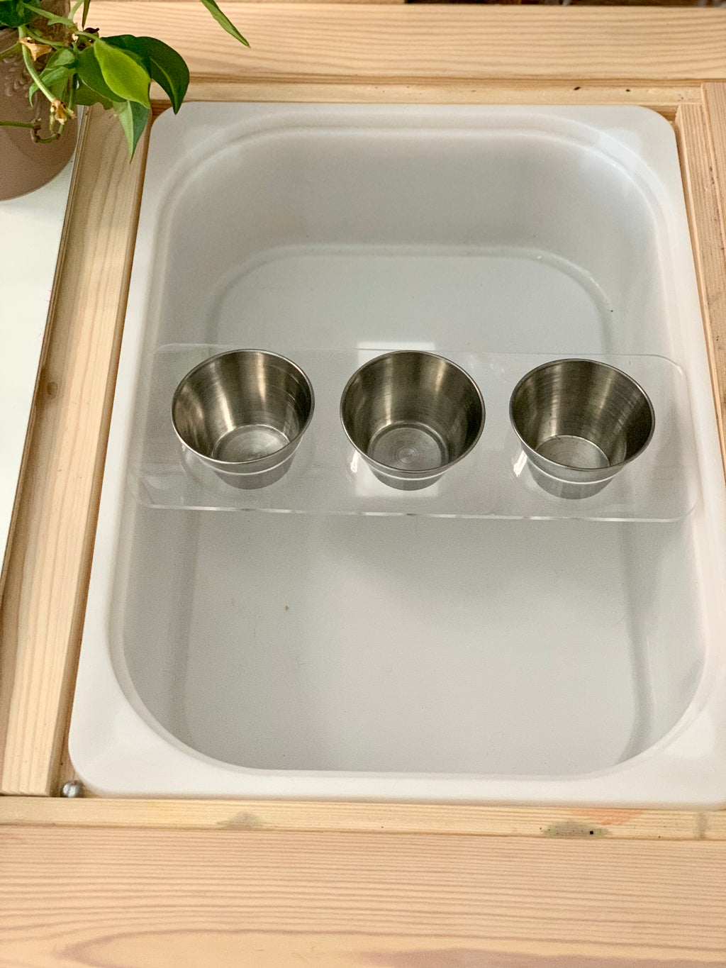 Wooden tabletop insert with clear acrylic cross piece holding three metal cups inside large Flisat bin insert