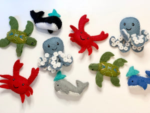 Assortment of handmade felt sea creatures including crabs, turtles, octopuses, whales, and sharks on white background