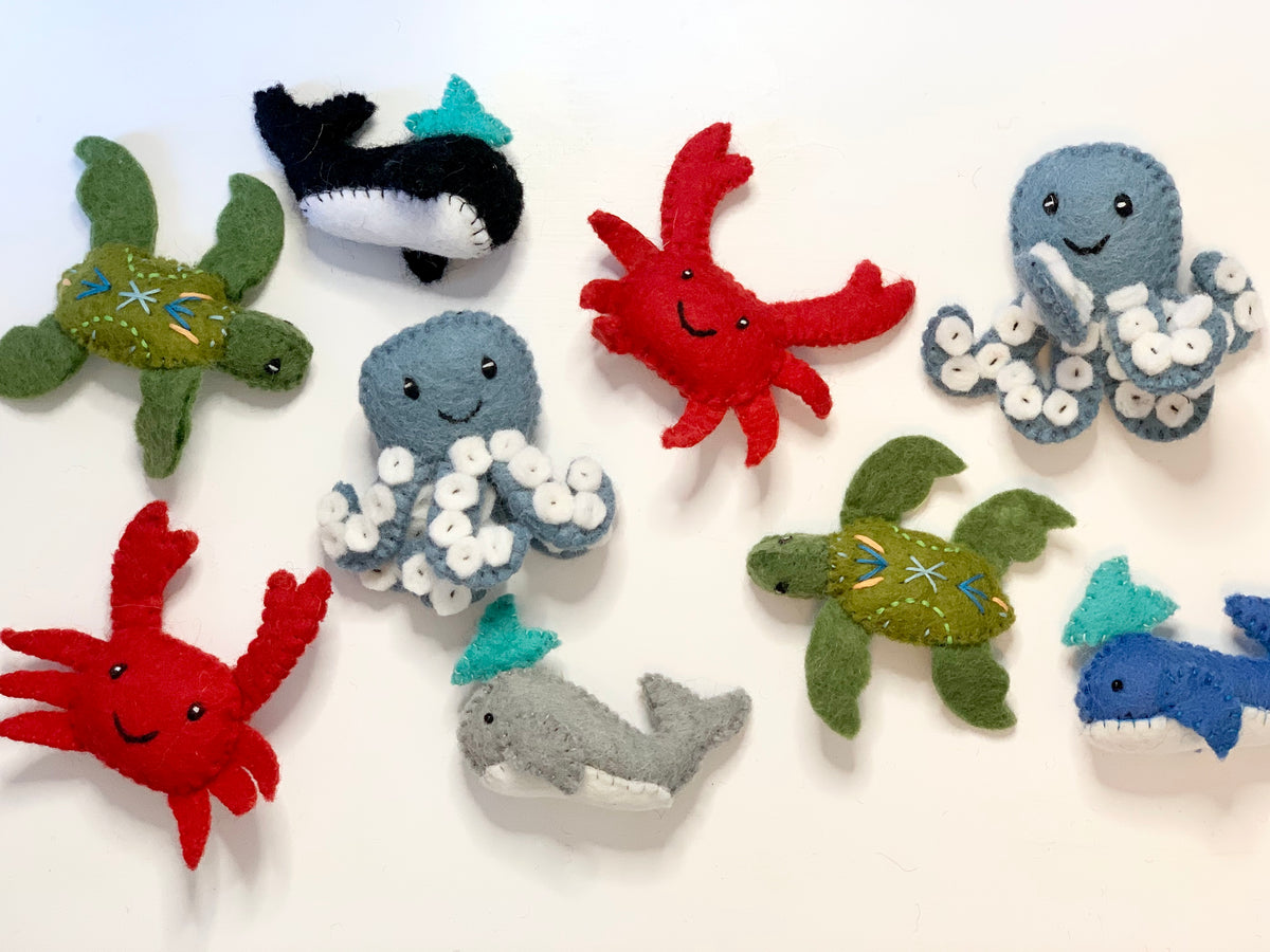 Assortment of handmade felt sea creatures including crabs, turtles, octopuses, whales, and sharks on white background