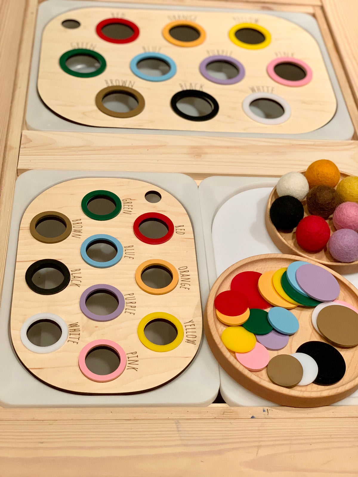Wooden color sorting boards with labeled painted holes, felt balls, and matching colored wooden discs on light wood surface