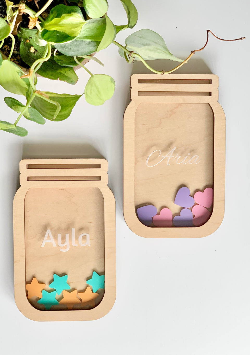 Two personalized wooden reward jars shaped like mason jars filled with pastel wooden tokens on white surface