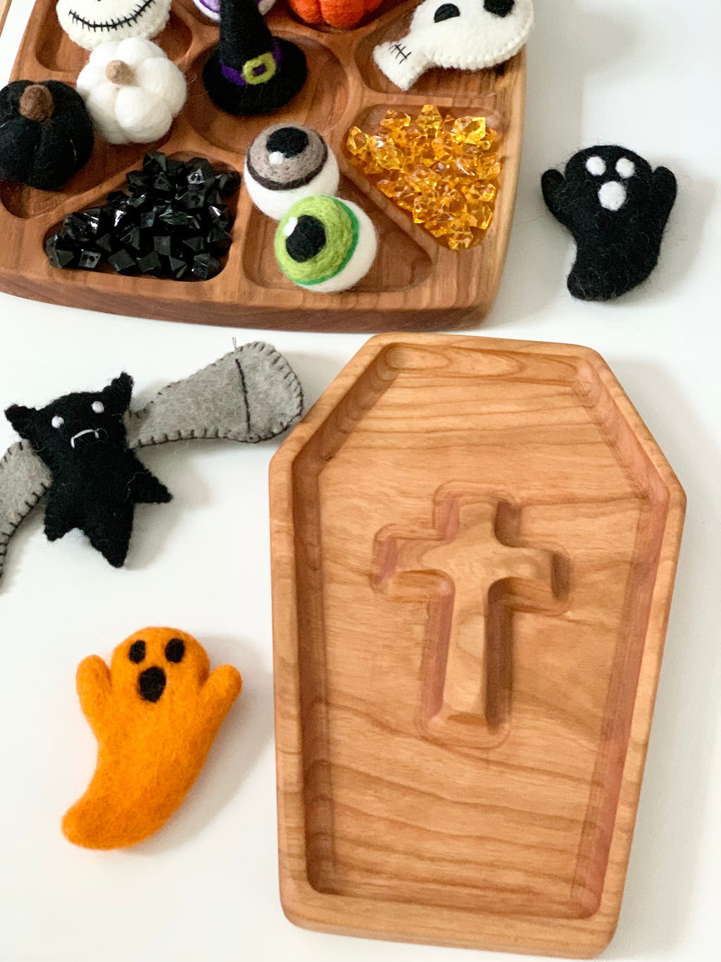 Wooden coffin-shaped sensory tray with cross cutout surrounded by felt Halloween figures on white surface
