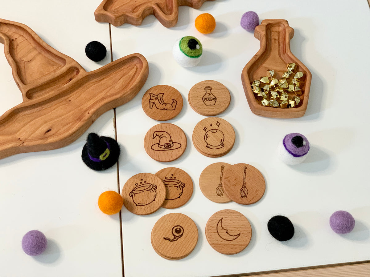 Hand drawn wooden witchy magic memory game pieces with engraved mystical symbols and colorful felt balls on white surface