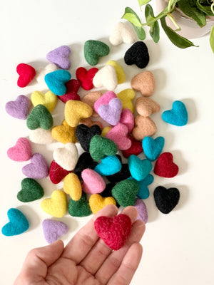 Colorful small handmade felt hearts in various colors with one red heart held in hand on white background