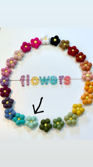 Circle of colorful felt flowers surrounding glittery resin letters spelling flowers on white background