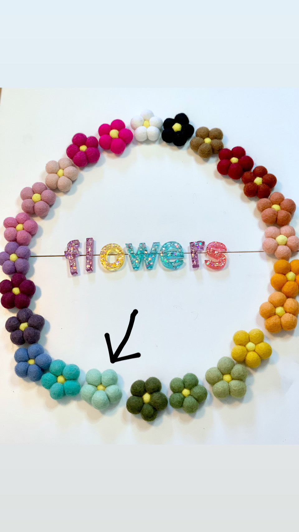 Circle of colorful felt flowers surrounding glittery resin letters spelling flowers on white background
