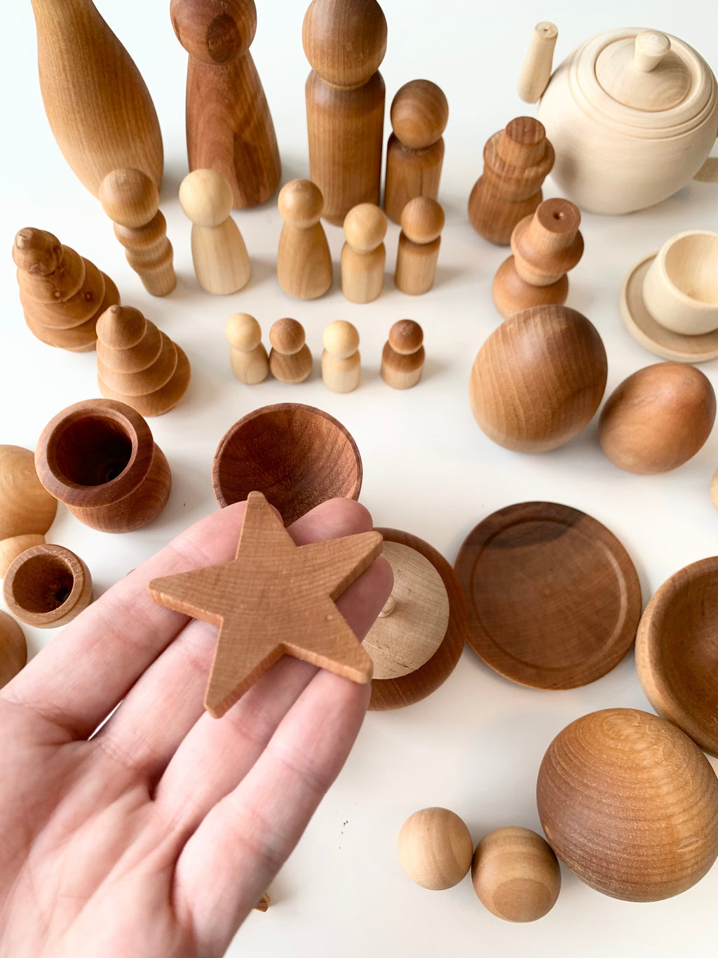 Hand holding small smooth wooden star among various natural wood shapes and bowls on white surface