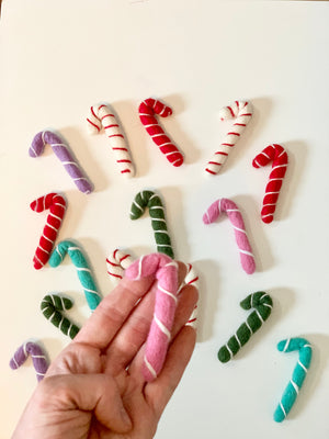 Hand holding one pink felt candy cane surrounded by red, green, purple, turquoise, and white felt candy canes on white background