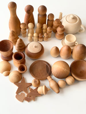 Variety of natural wood toys and figures including bowls, peg dolls, eggs, and decorative shapes on white background