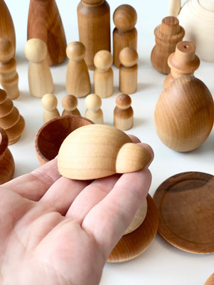 Hand holding small smooth unfinished wooden turtle figure with various natural wood shapes and bowls on white surface