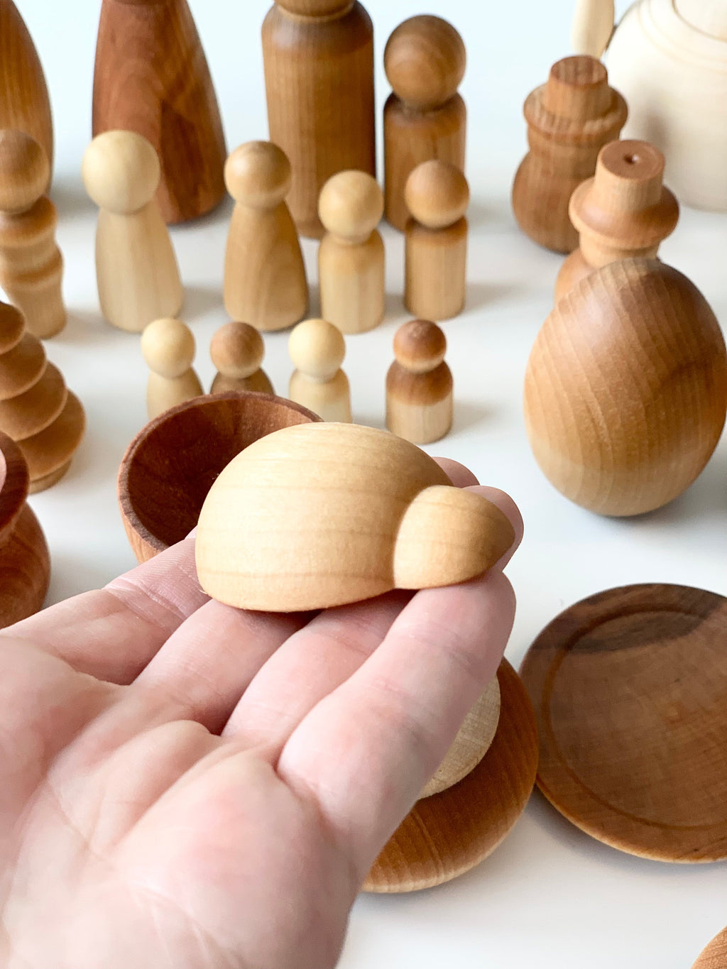 Hand holding small smooth unfinished wooden turtle figure with various natural wood shapes and bowls on white surface