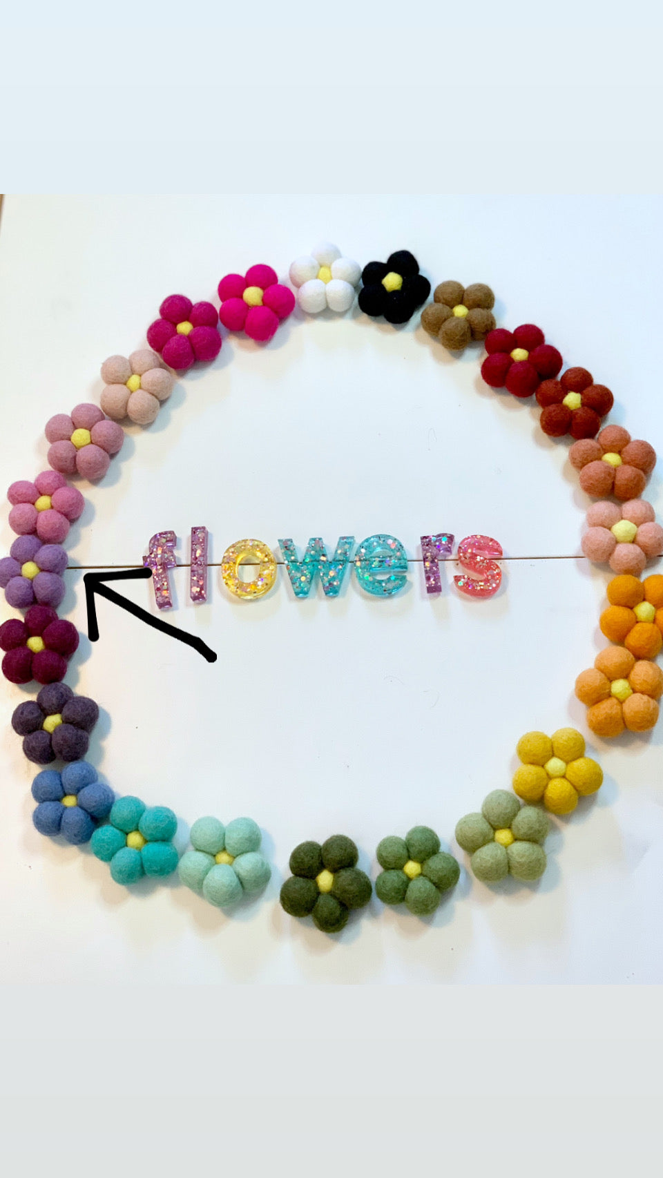 Colorful handmade single felt flowers arranged in a circle around glittery letters spelling flowers on white background