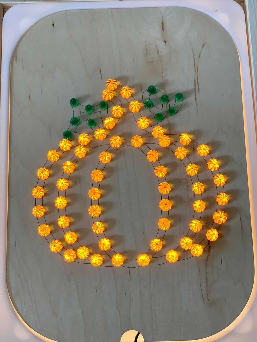 Wooden Flisat insert with orange and green light-up pegs arranged in a pumpkin shape on light wood background