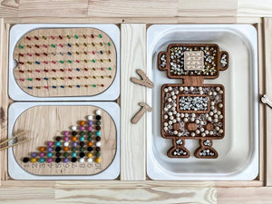 Wooden robot-shaped sensory tray with wooden pegboard, colorful beads, and sorting trays on natural wood surface