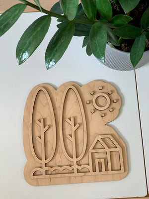 Maple wood play tray shaped like a house with trees and sun design on white table near green plant