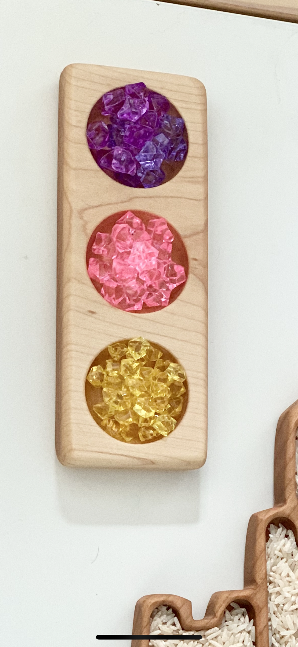 Wooden traffic light sensory tray filled with purple, pink, and yellow translucent sensory beads on white surface