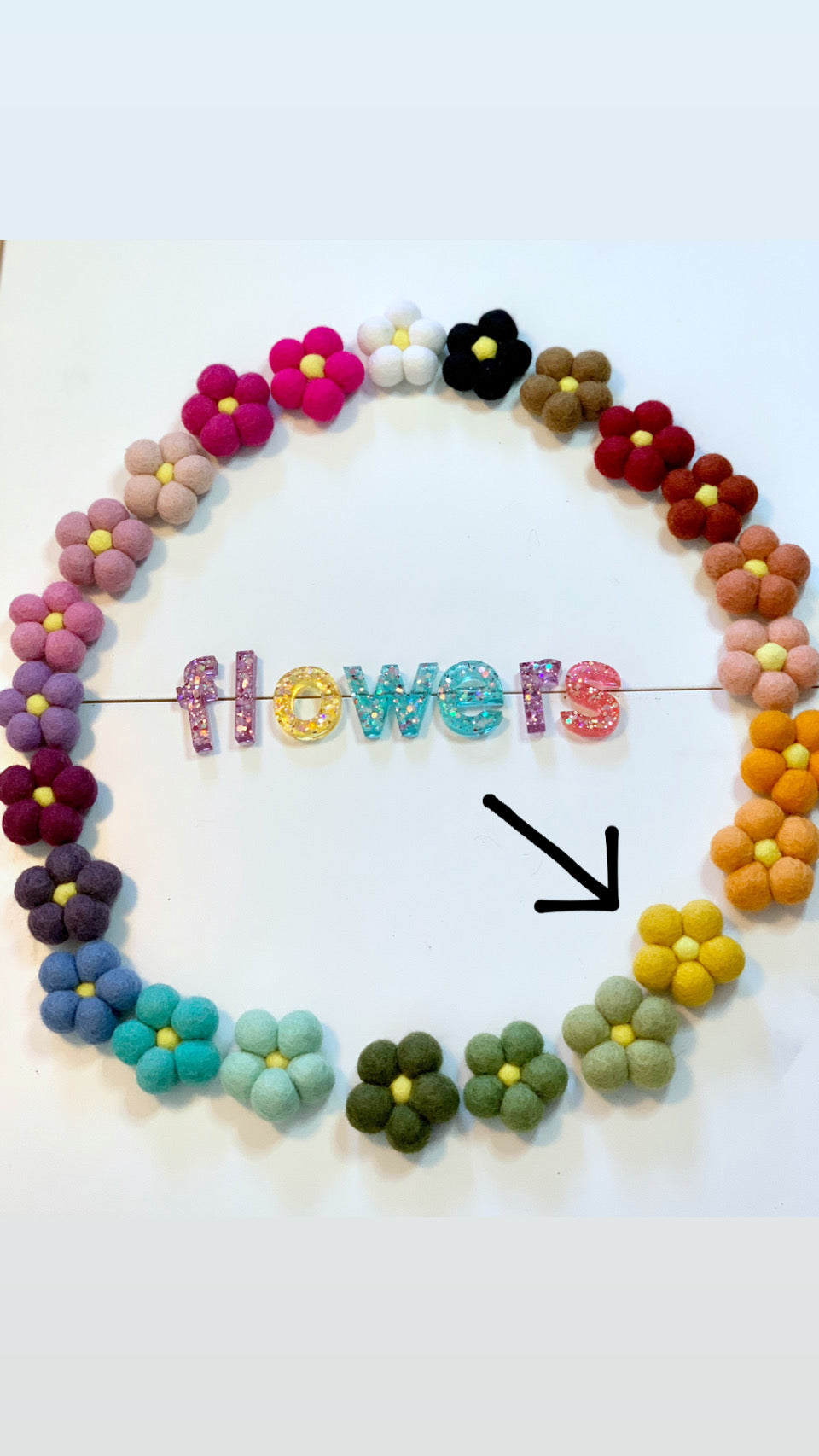 Circle of colorful handmade felt flowers arranged around glittery letters spelling flowers on white background