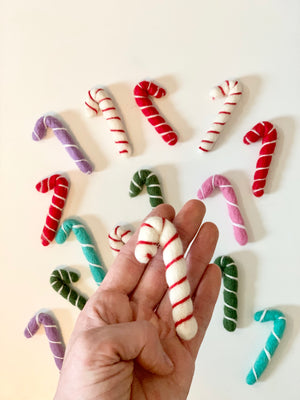 Hand holding single white felt candy cane with red stripes surrounded by various colored felt candy canes on white surface