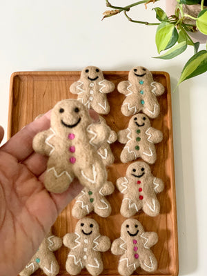 Hand holding one felt gingerbread person with colorful buttons above wooden tray filled with similar felt gingerbread figures