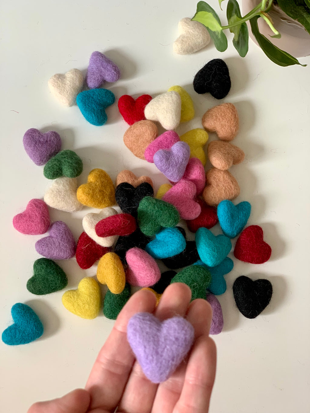 Assortment of small colorful handmade felt hearts scattered on white surface with one held in hand close-up