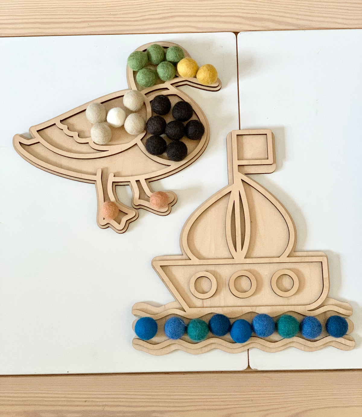 Fillable duck and boat play trays with colorful felt balls on light wood and white surface