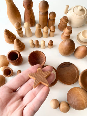 Hand holding small natural wood star shape with various smooth wooden figures and bowls on white surface
