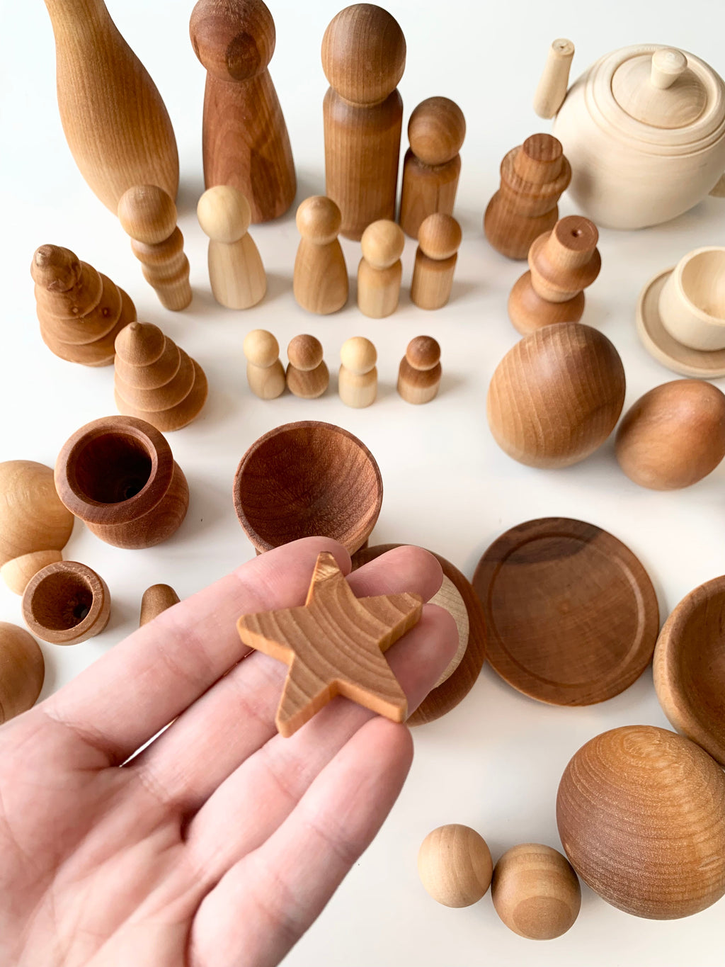 Hand holding small natural wood star shape with various smooth wooden figures and bowls on white surface