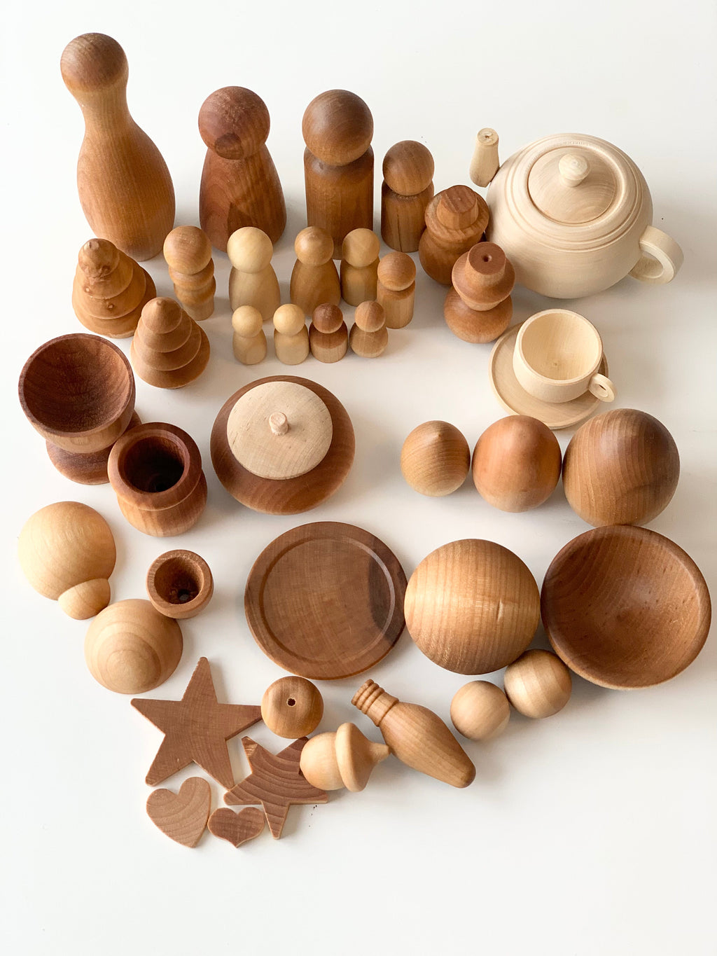 Assorted smooth natural wood pieces including peg dolls, spheres, bowls, a teapot, and cutout shapes on white background