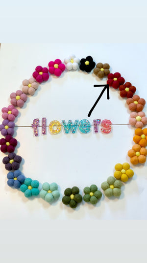 Single red felt flower among multicolored felt flowers arranged in a circle on white background