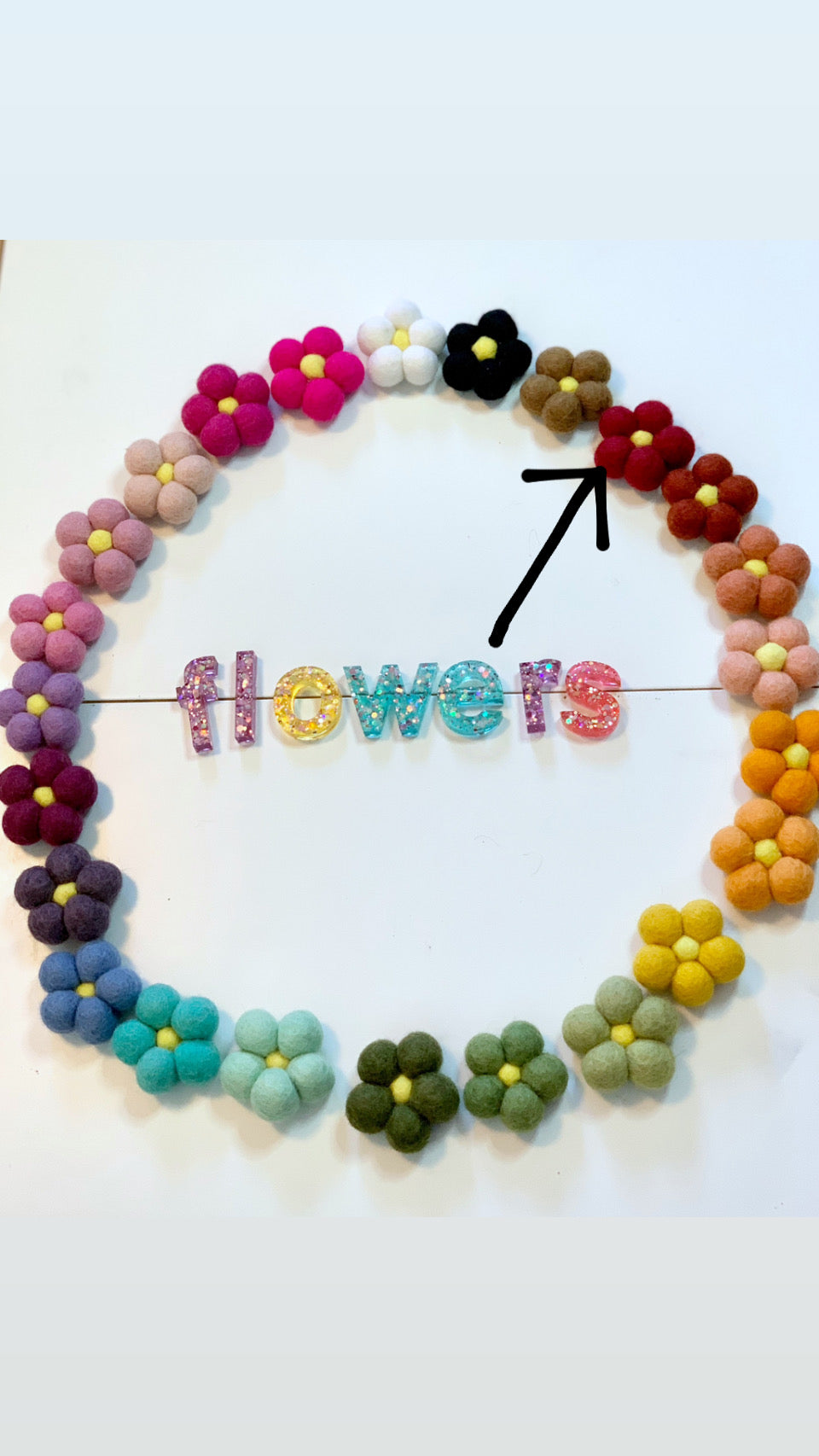 Single red felt flower among multicolored felt flowers arranged in a circle on white background