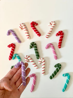 Hand holding a purple felt candy cane with more small handmade felt candy canes in various colors on white background