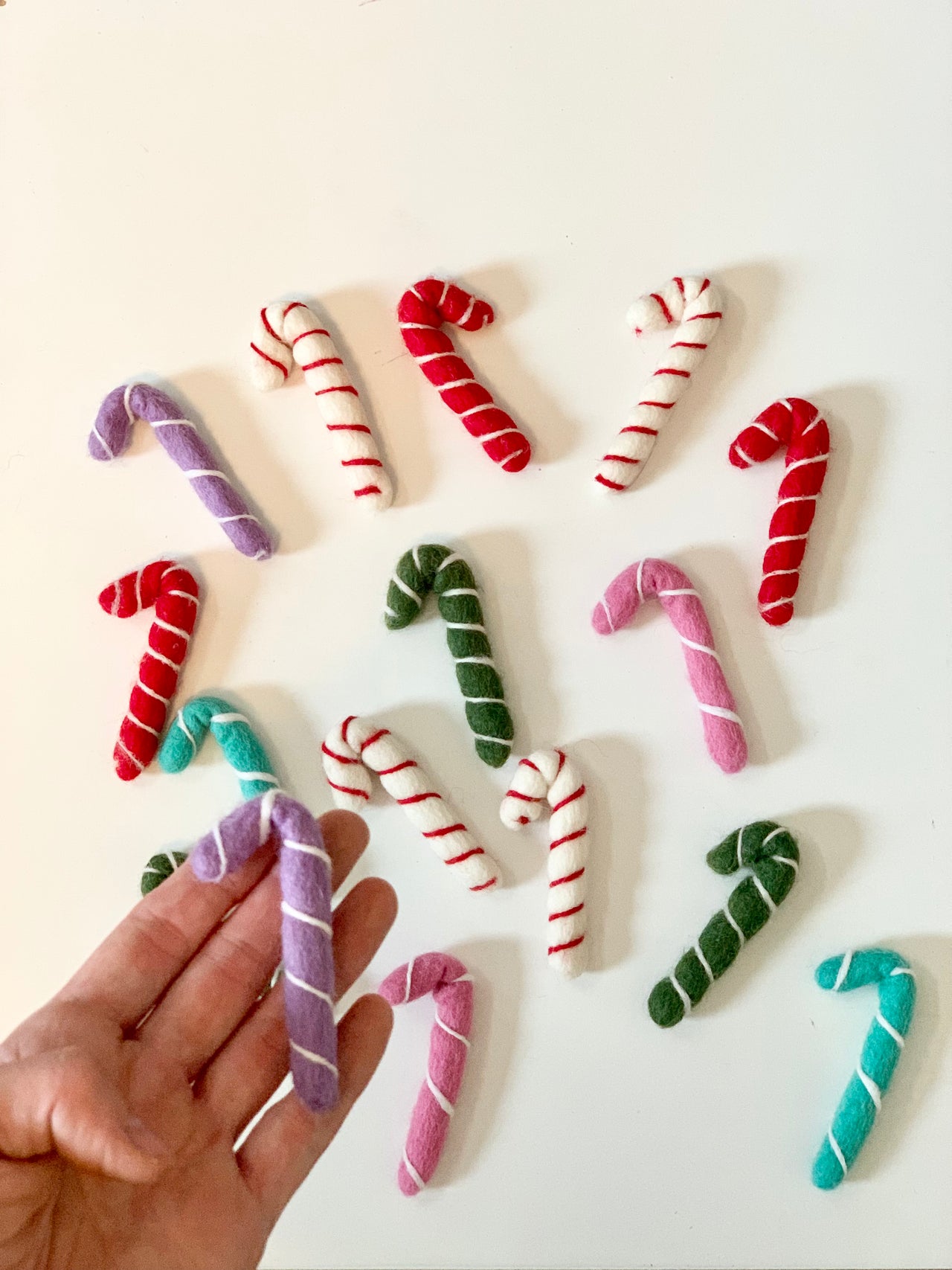 Hand holding a purple felt candy cane with more small handmade felt candy canes in various colors on white background