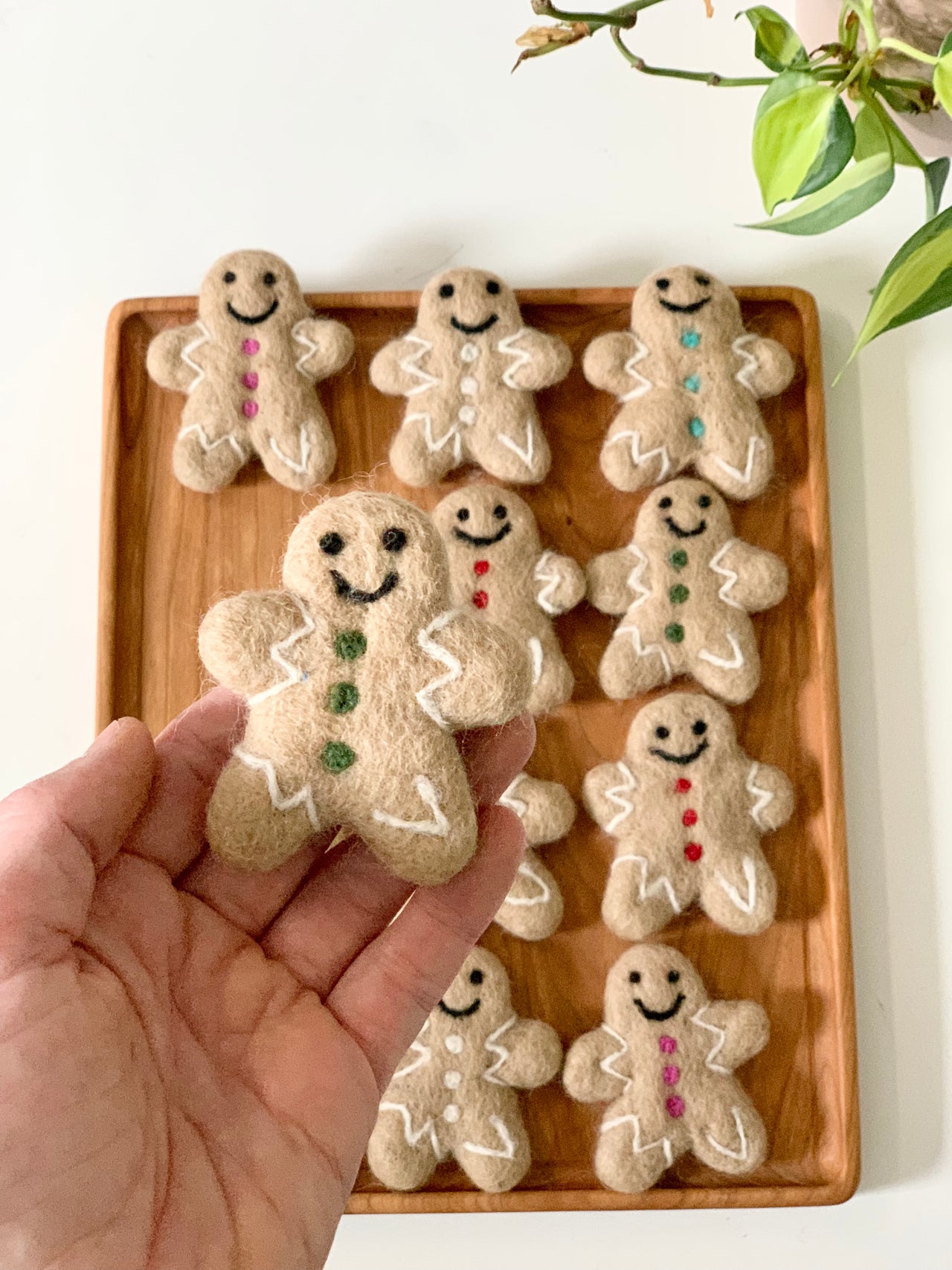 Handmade felt gingerbread person with green buttons and white icing details held above wooden tray with similar figures