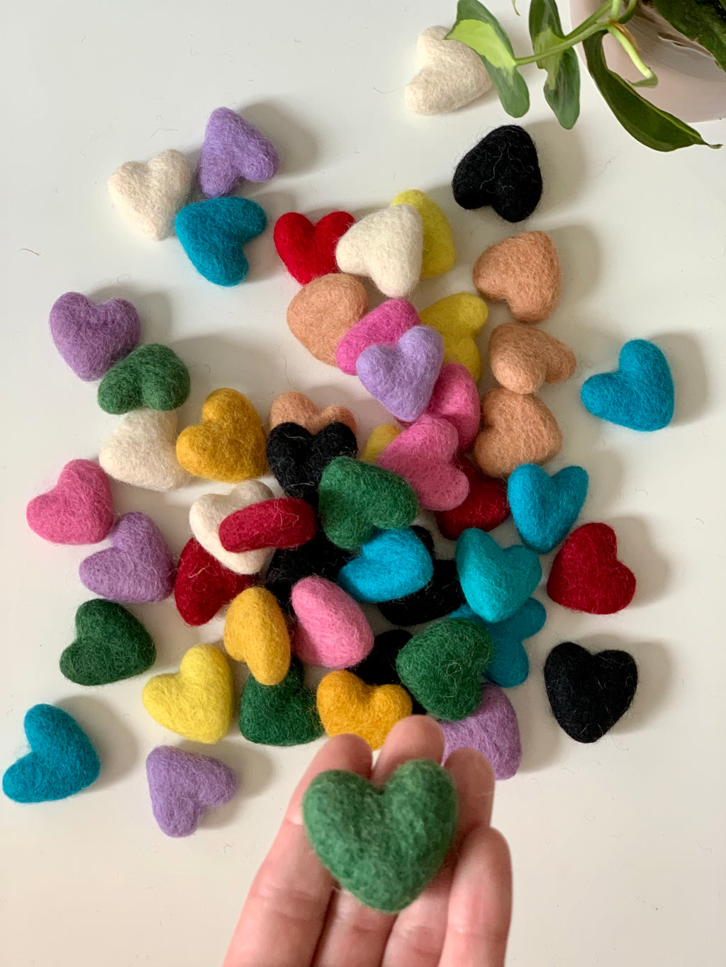 Assorted small felt hearts in various colors scattered on white surface with hand holding green heart