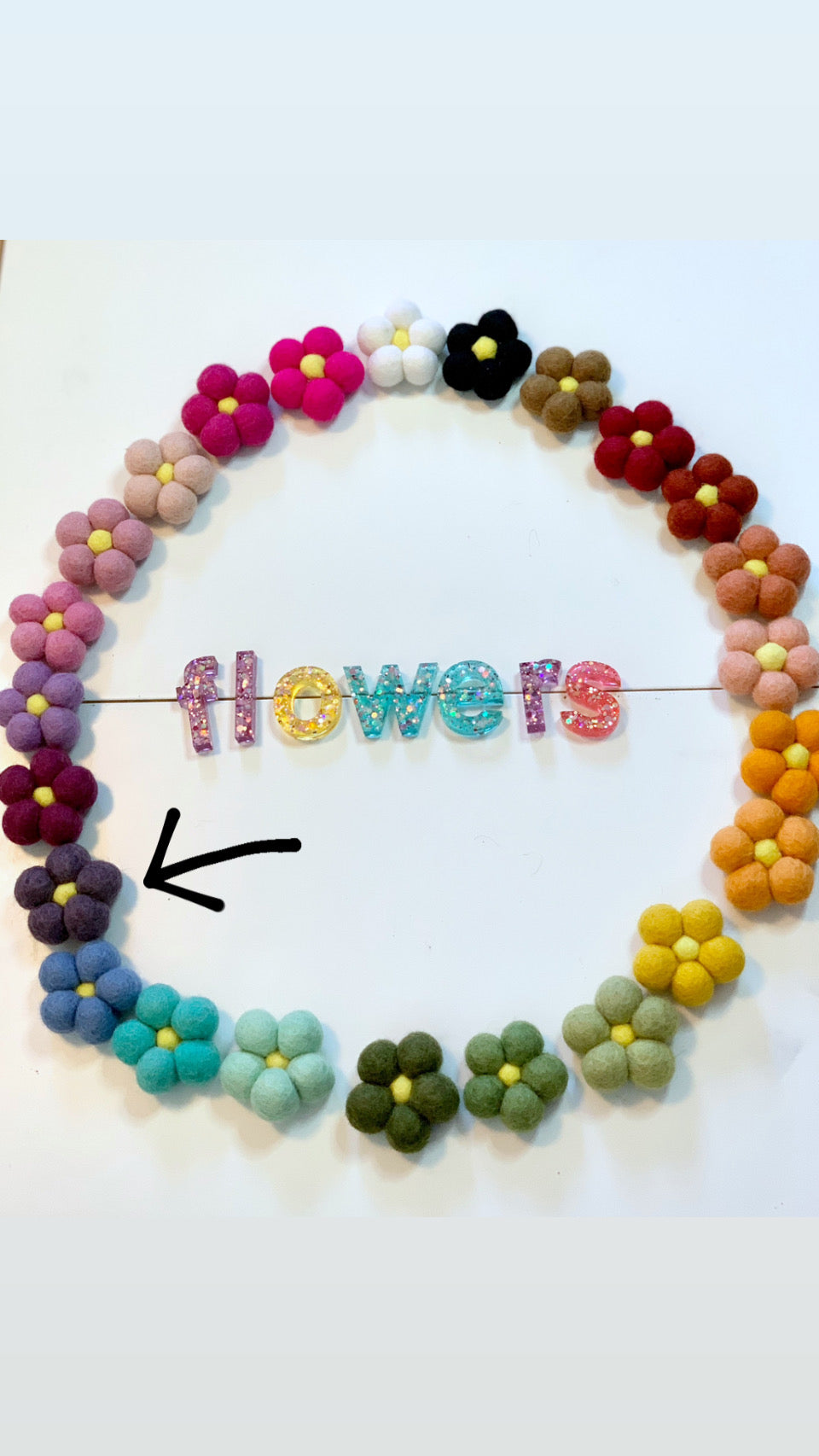 Assorted colorful handmade felt flowers arranged in a circle with glittery letters spelling flowers on white background