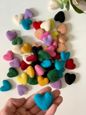 Colorful small handmade felt hearts in various colors scattered on white surface with one held in hand